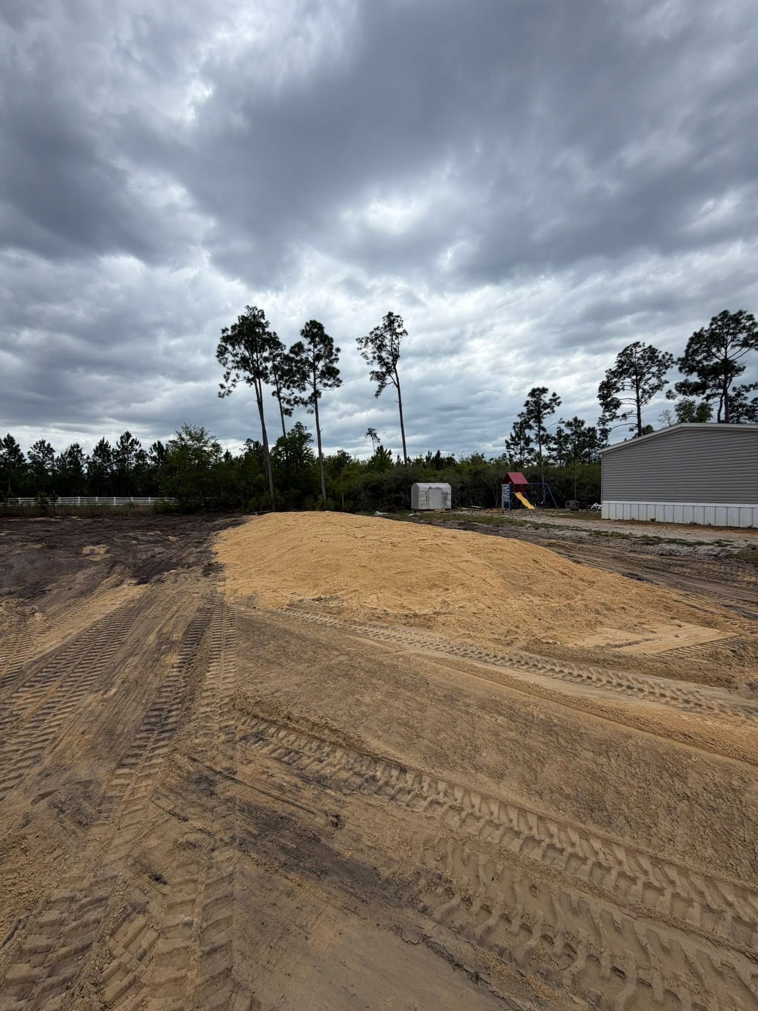Dirt road under dark storm clouds with a worker and white tent at a construction site