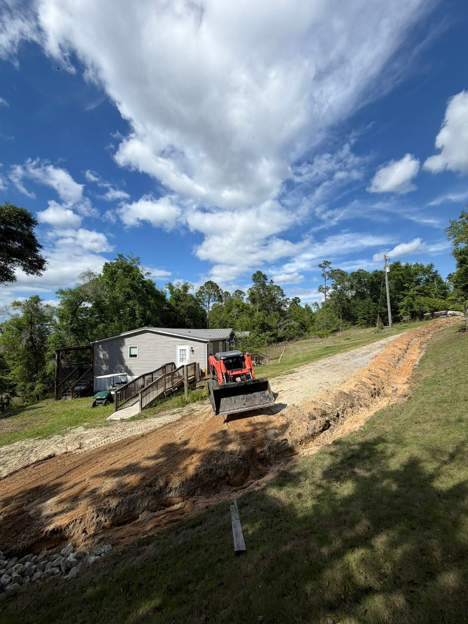 Construction equipment grading a dirt hillside beside a gray trailer under a blue sky