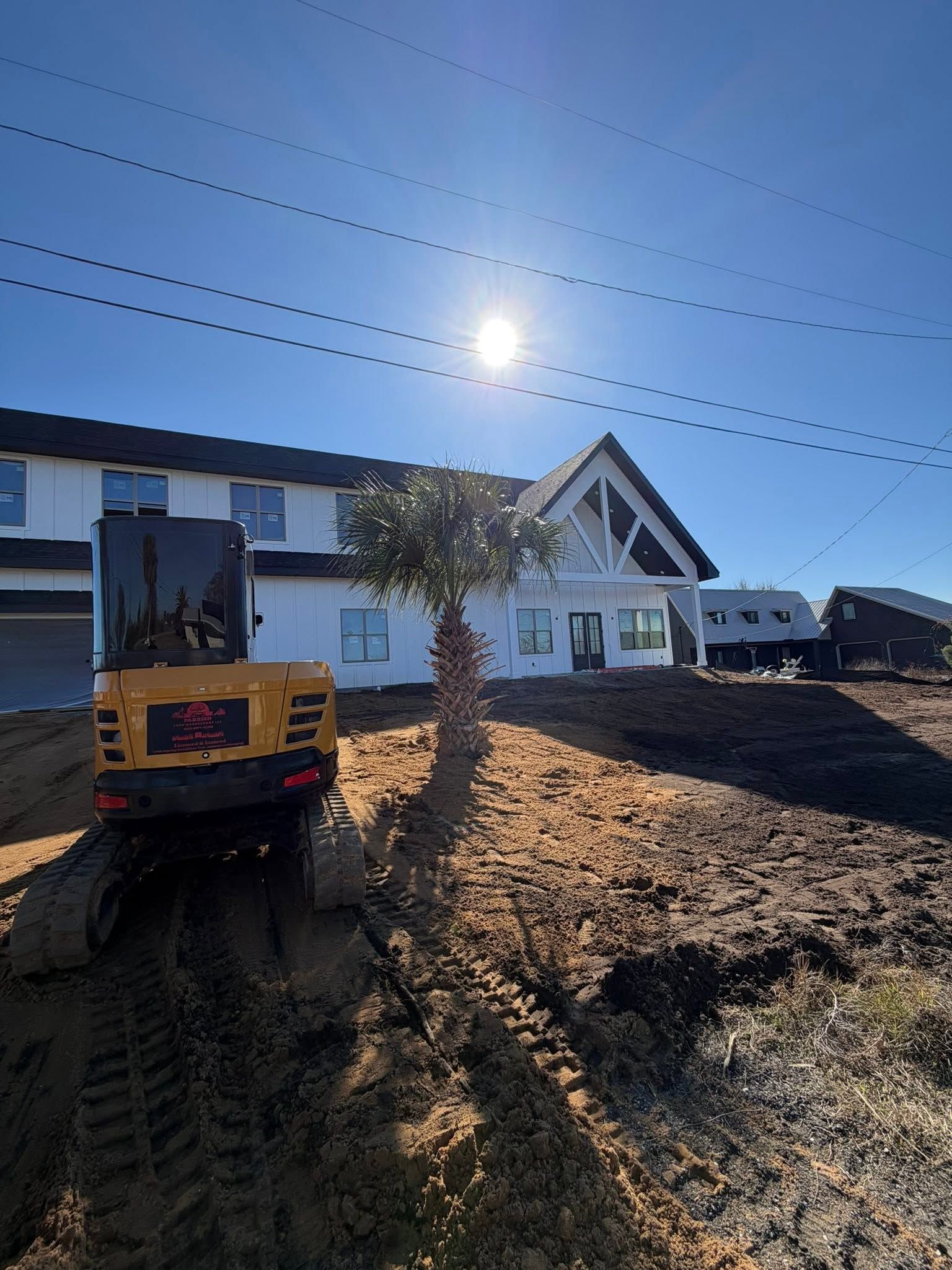 Construction site with excavator beside a white house under a bright blue sky