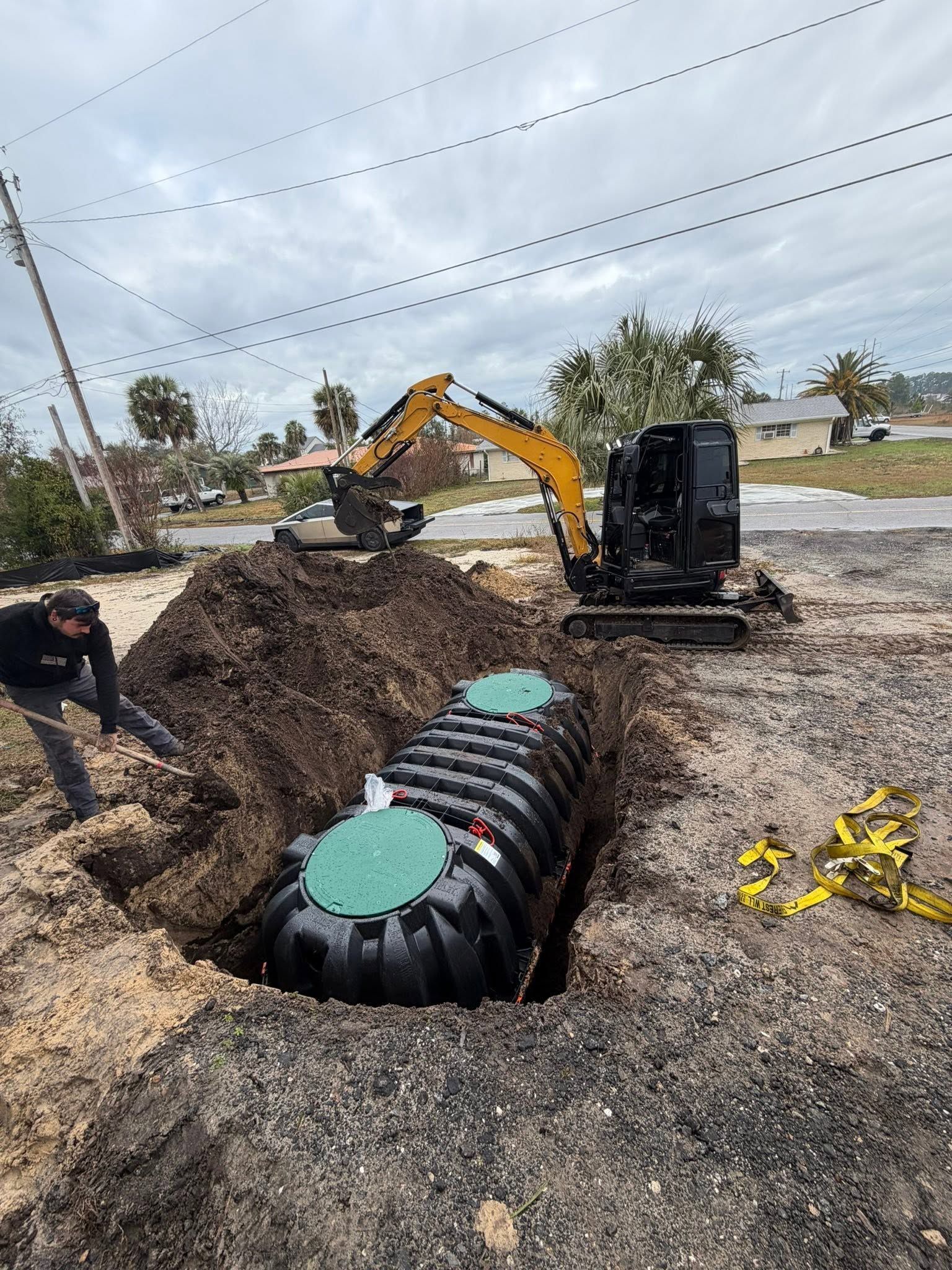 Construction site with excavator over a large black underground tank in an open dirt trench