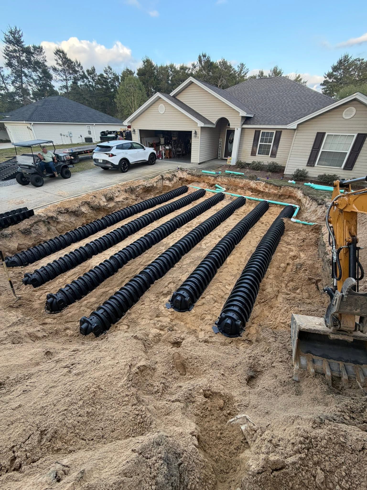 Construction site with black drainage pipes laid in rows in a front yard beside a house under renovation.