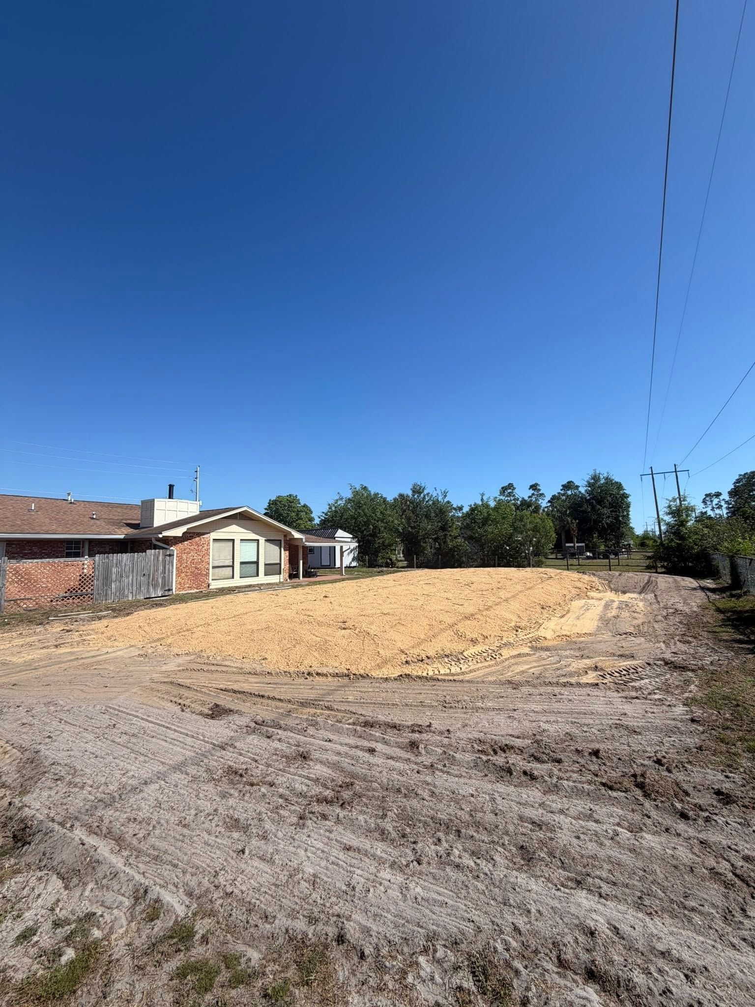 Cleared lot beside houses under a bright blue sky, with dirt and gravel foreground.