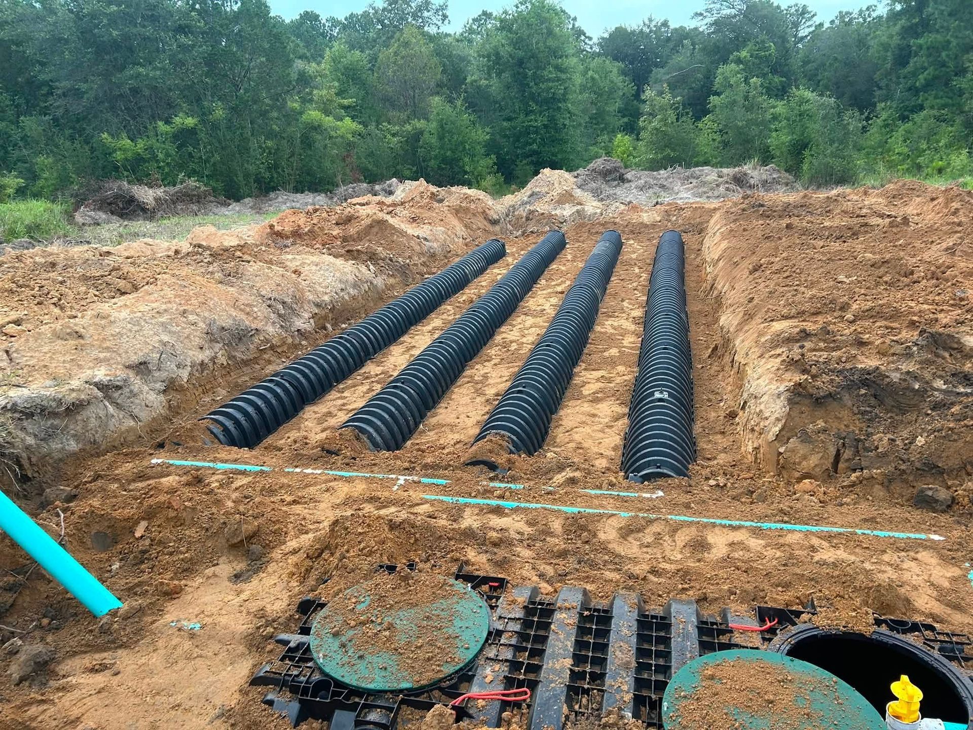 Black corrugated pipes laid in parallel in a dirt trench at a wooded construction site