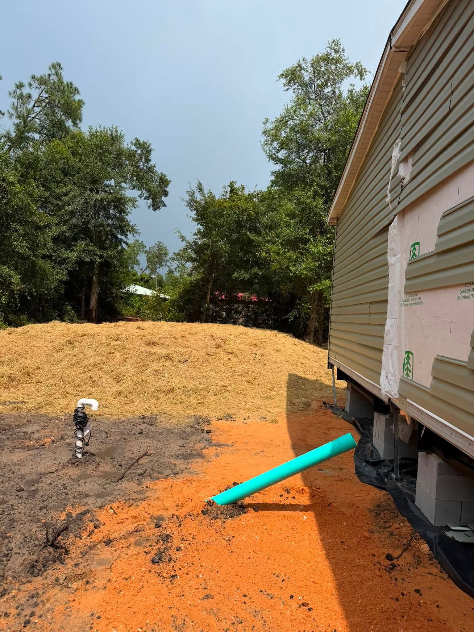 Orange gravel beside a house with a turquoise drainpipe and a worker in the background