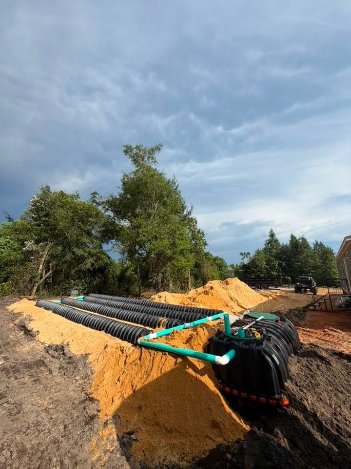 Black drainage pipes laid in a sandy trench at an outdoor construction site under a cloudy sky