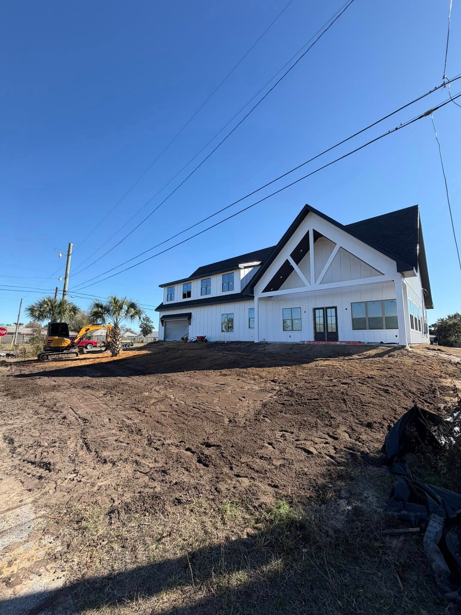New white house with dark roof on a dirt lot under a clear blue sky