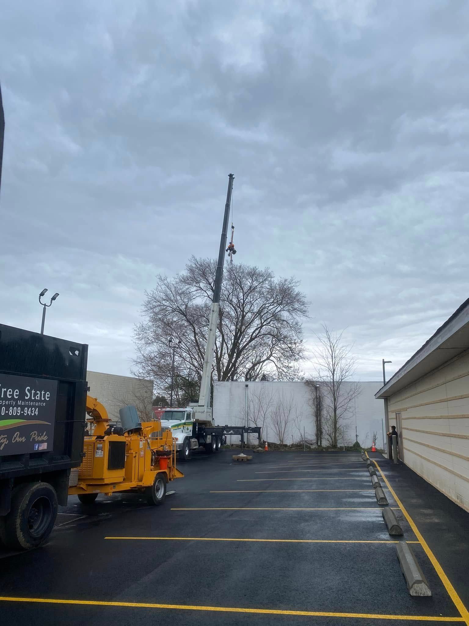 Parking lot with yellow utility truck, tall pole lift, and white building under cloudy sky