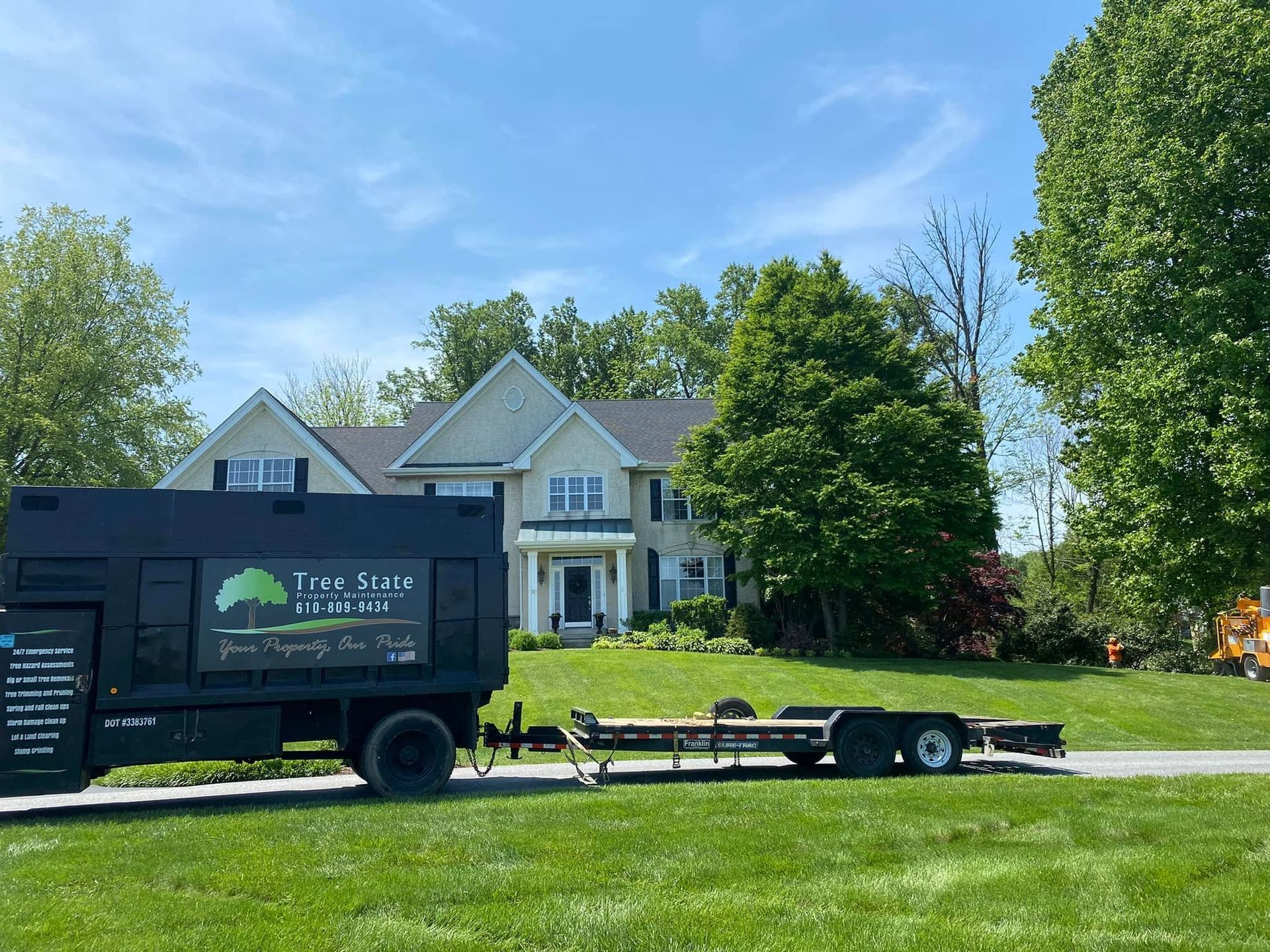 Black landscaping truck and trailer in front of a large beige house on a sunny suburban lawn
