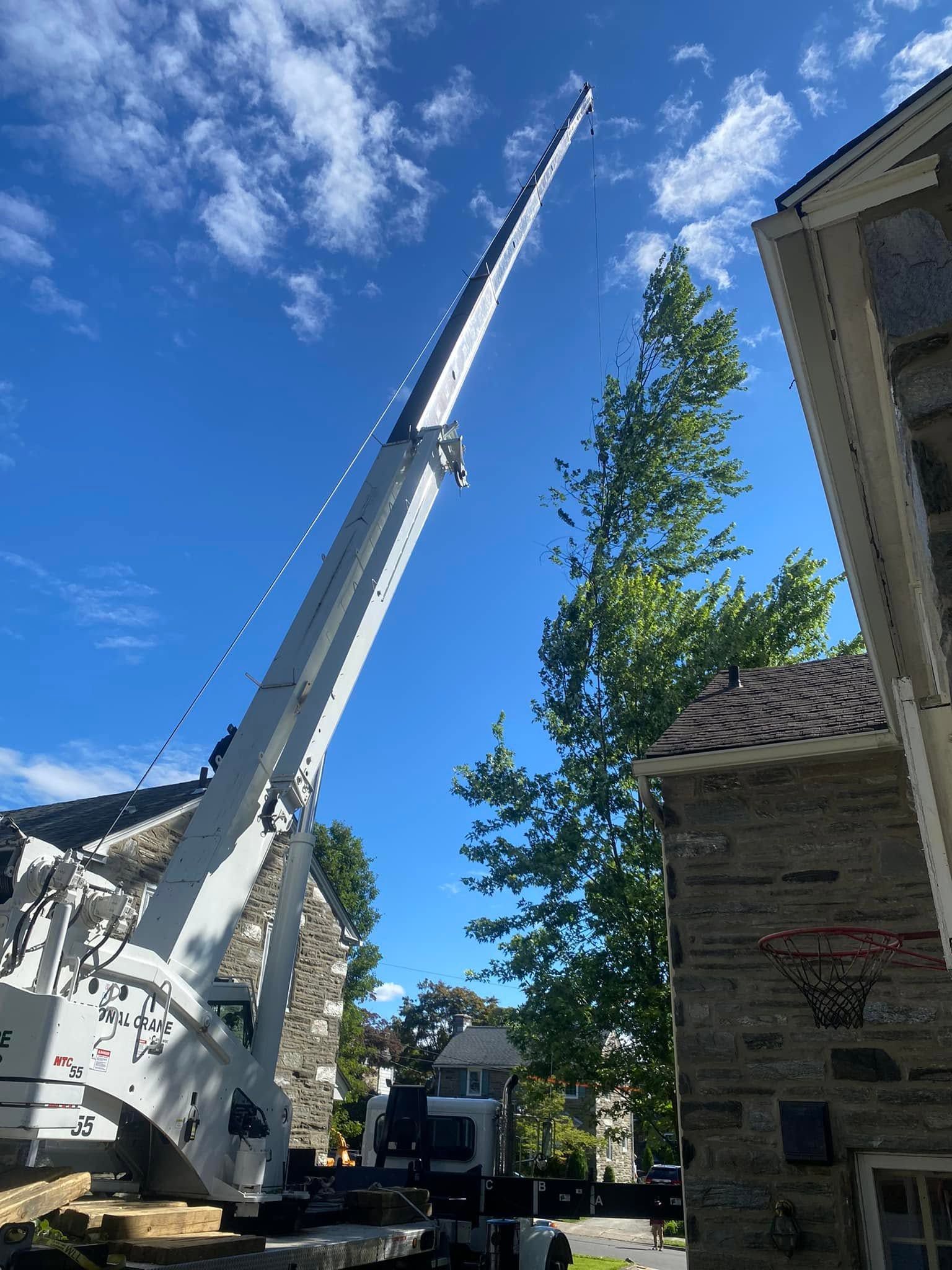 Crane with extended boom beside a house under a bright blue sky and clouds