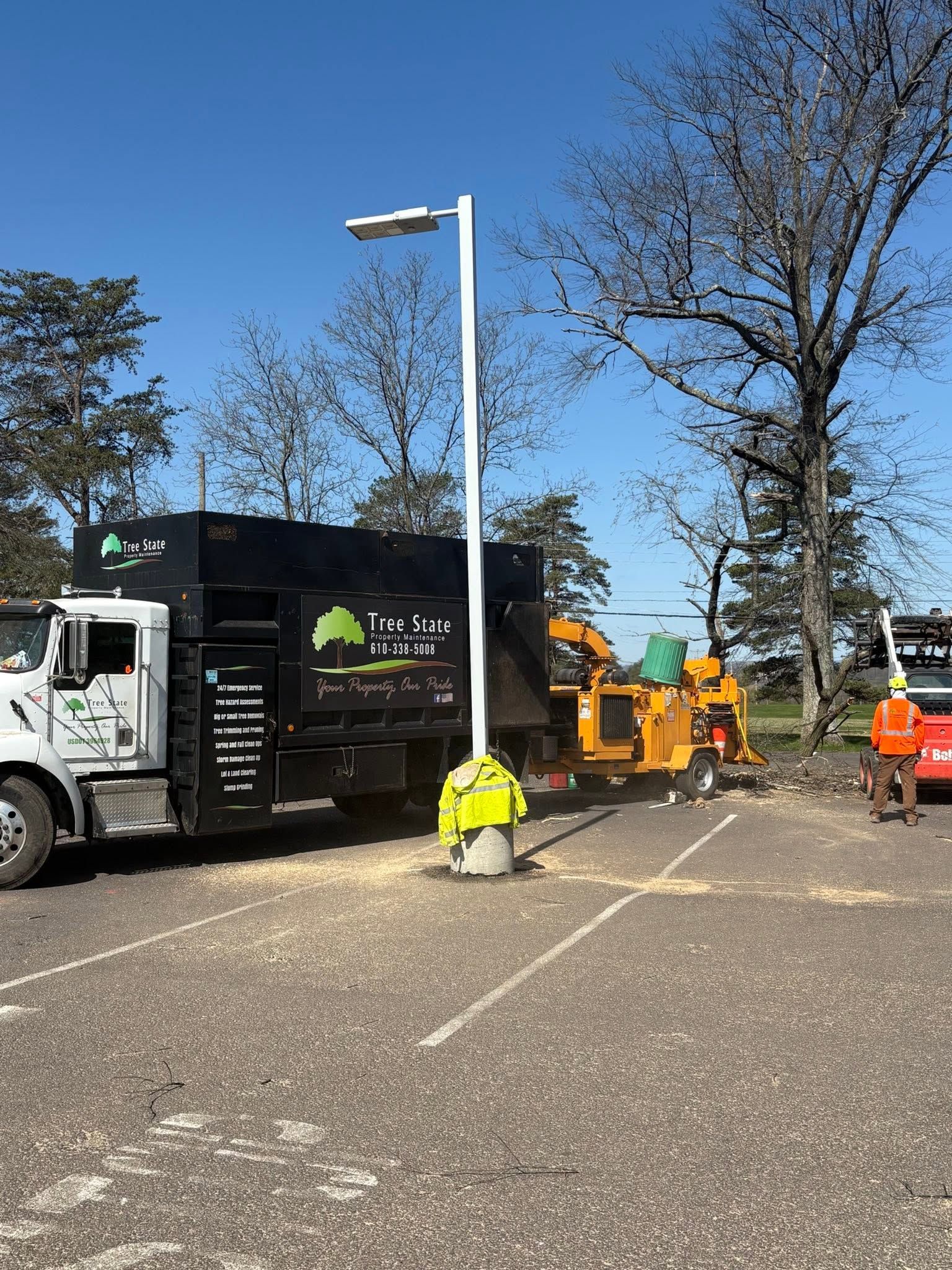 Roadwork crew beside a black utility truck and orange machinery on a sunny street