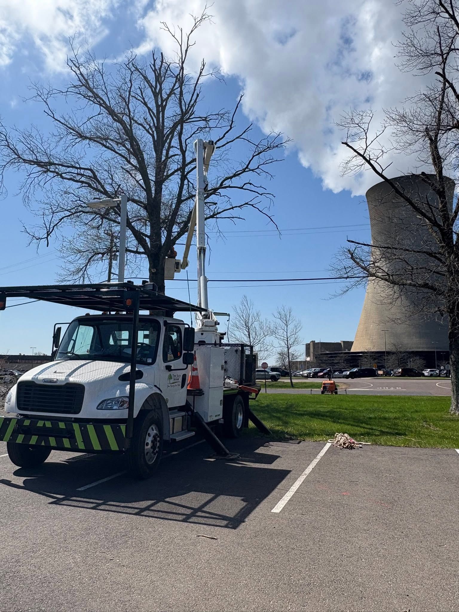 Utility truck parked beside a windmill on a sunny day, with workers nearby and leafless trees in the background