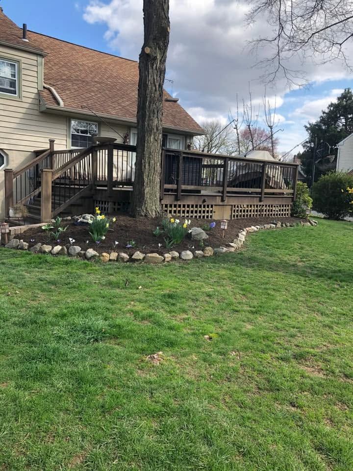 House with raised wooden deck, staircase, and landscaped yard with a large tree in the foreground.