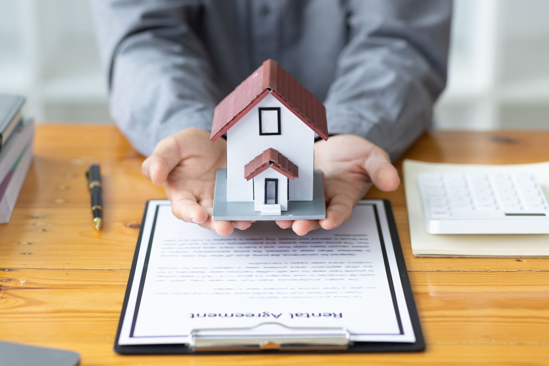 A man is holding a model house in his hands over a clipboard.