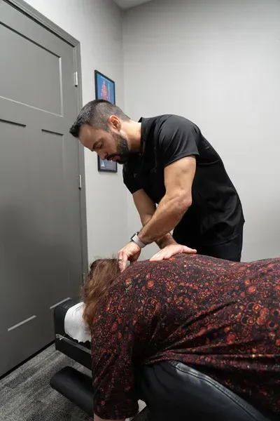 Chiropractor adjusting a patient's neck in an office. The patient is lying down. The chiropractor wears black.