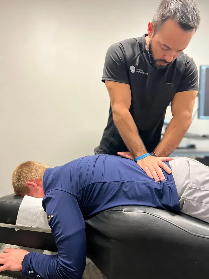 Chiropractor performing back adjustment on a patient lying face down on an examination table.