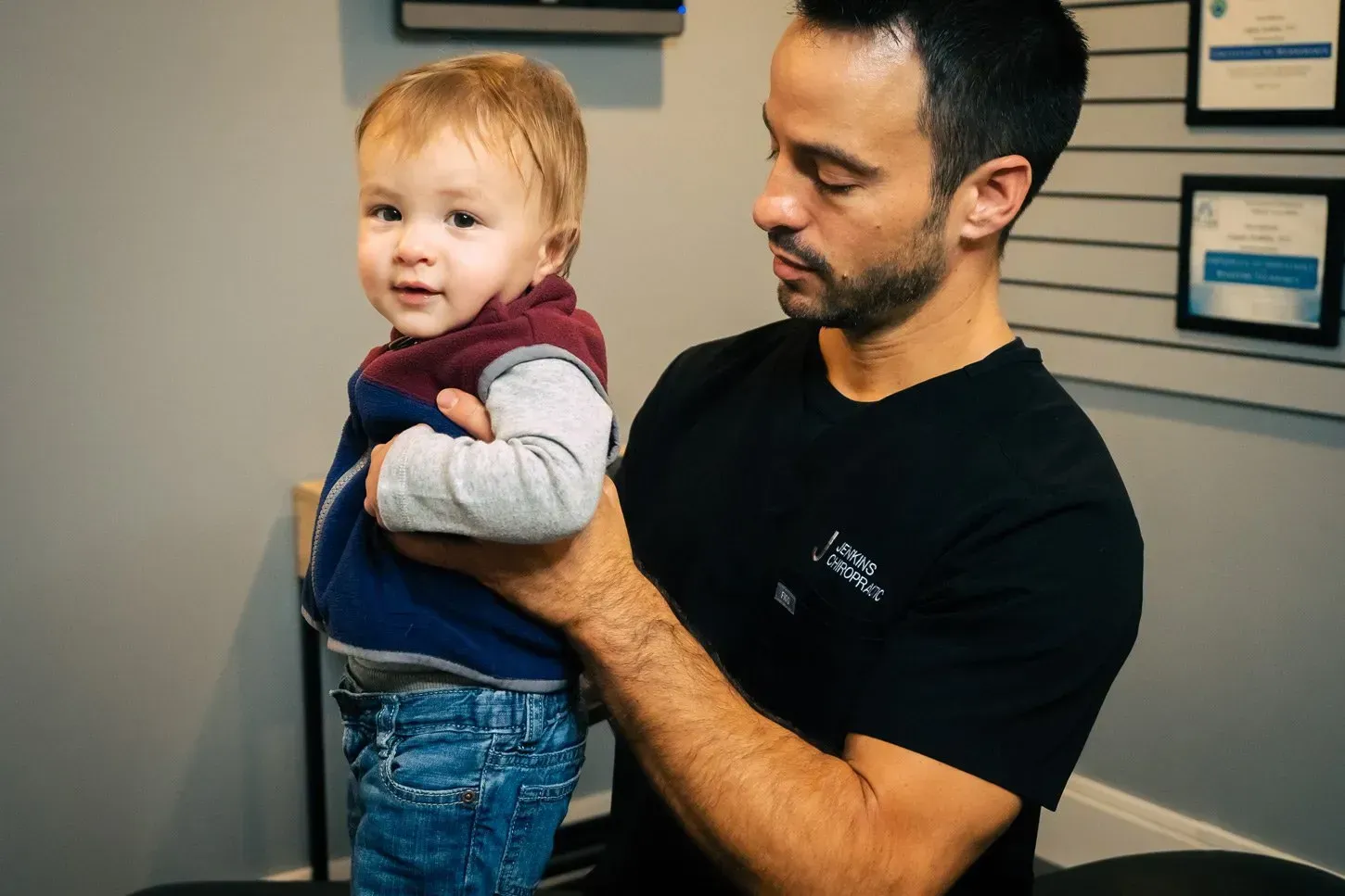 Man holding a toddler; both are in an office setting. The toddler is looking at the camera.