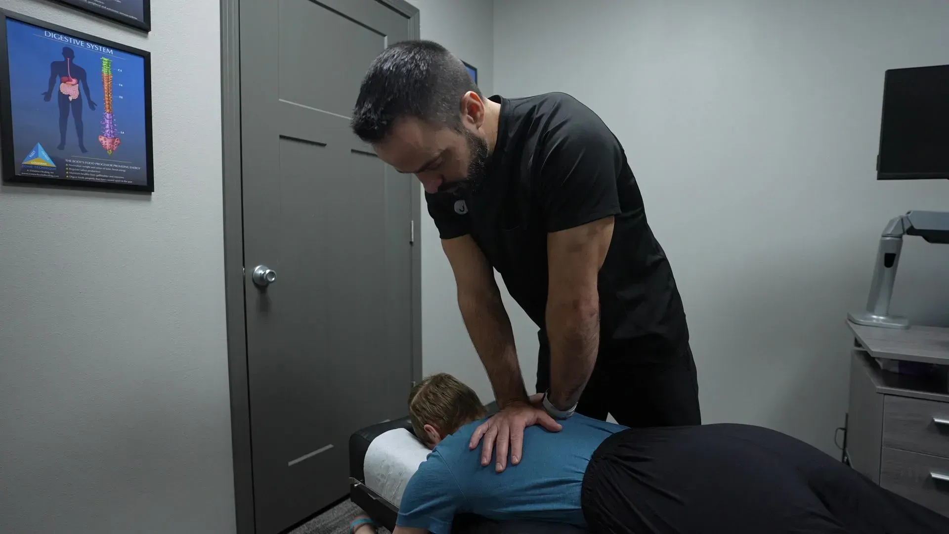 Chiropractor adjusting a patient's back on a treatment table in an office setting.