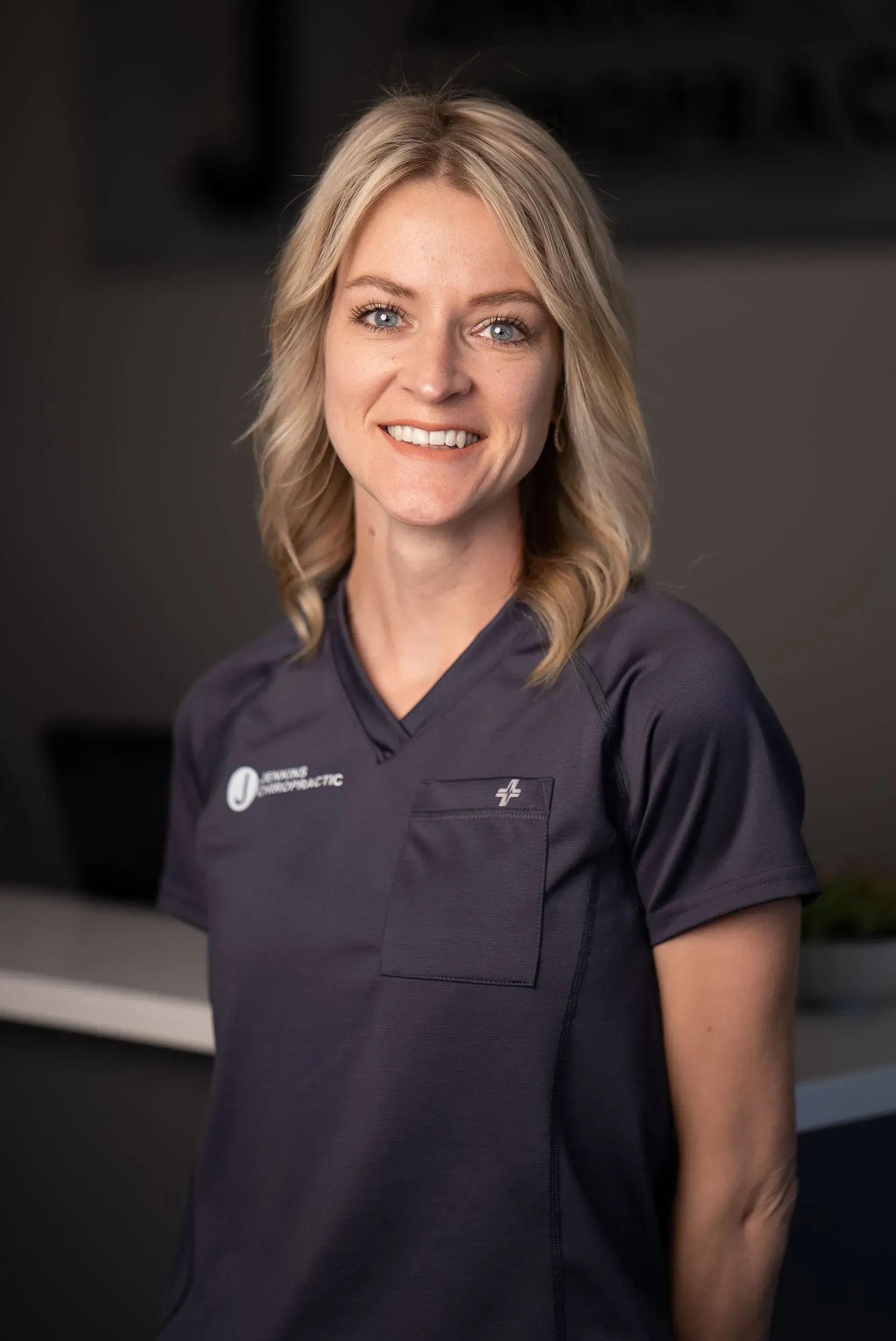 Woman in blue scrubs smiles at the camera in a professional setting.