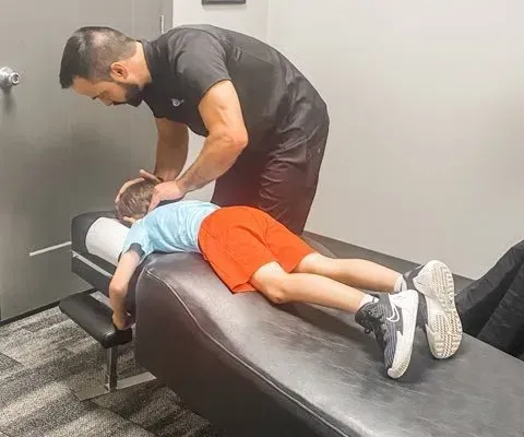 Chiropractor adjusting a child's neck on a treatment table in a clinical setting.