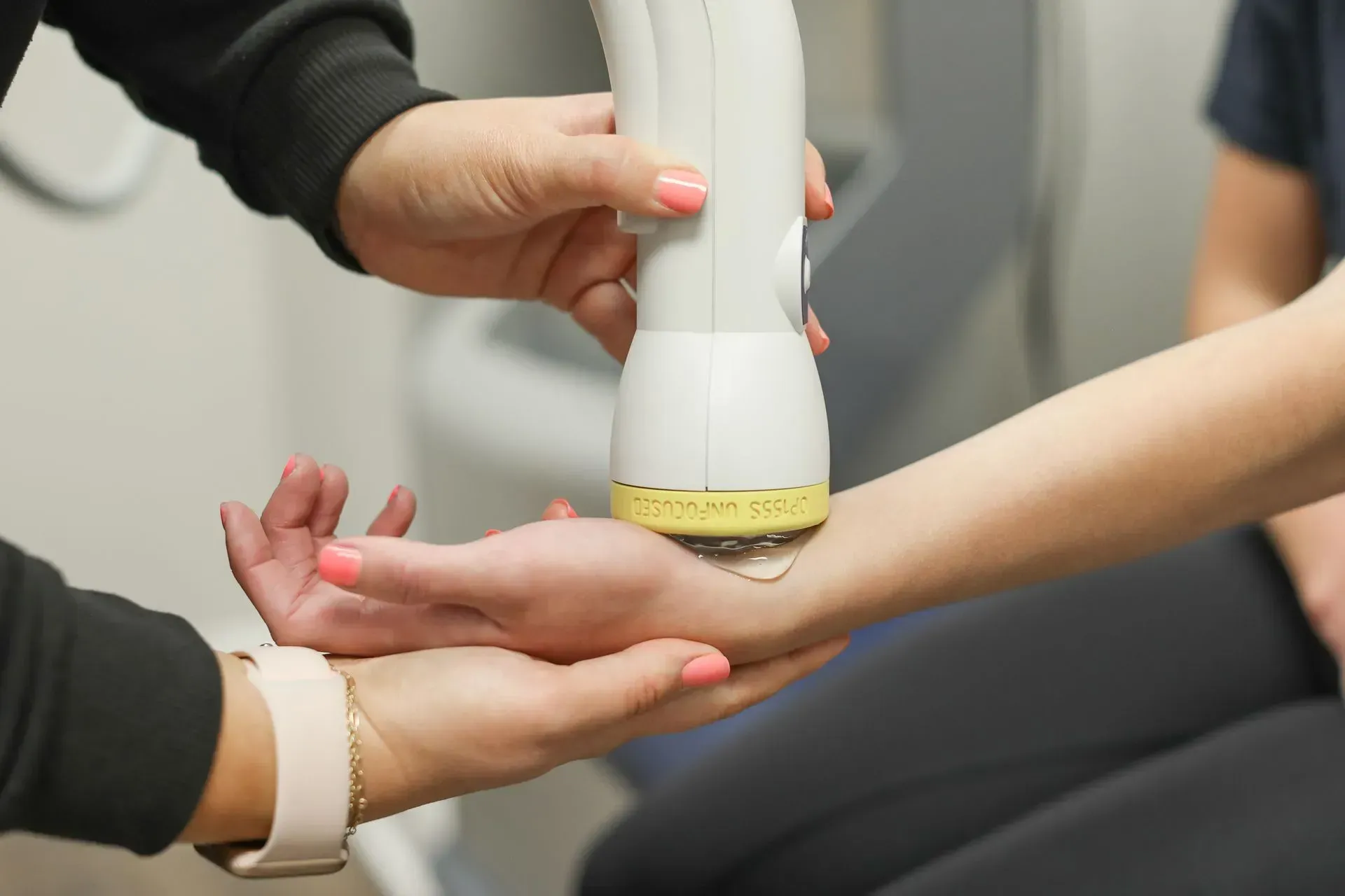 Person receiving medical treatment on wrist with a device, hands visible, light skin tone.