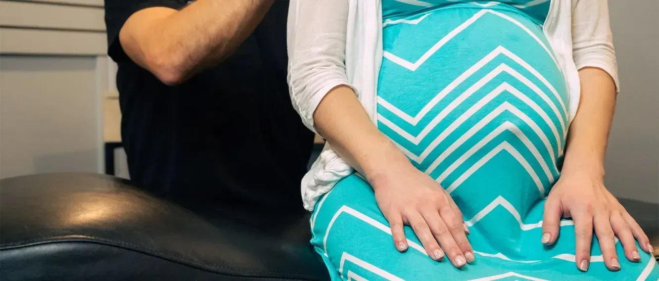 Pregnant person in teal dress, seated with another person, possibly at a medical appointment.