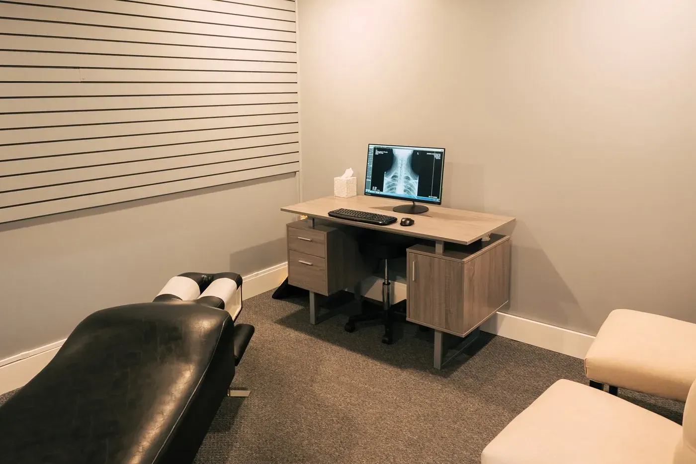 Chiropractor's office: table with monitor displaying x-ray, adjustment table, and seating. Neutral tones.