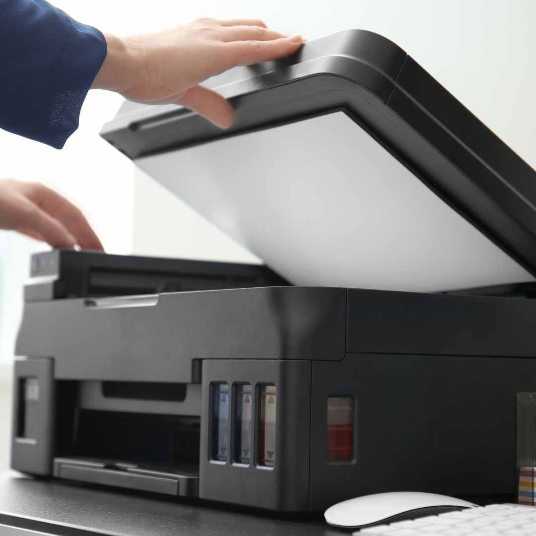 Person placing a sheet of paper on the glass scanner of a black printer.