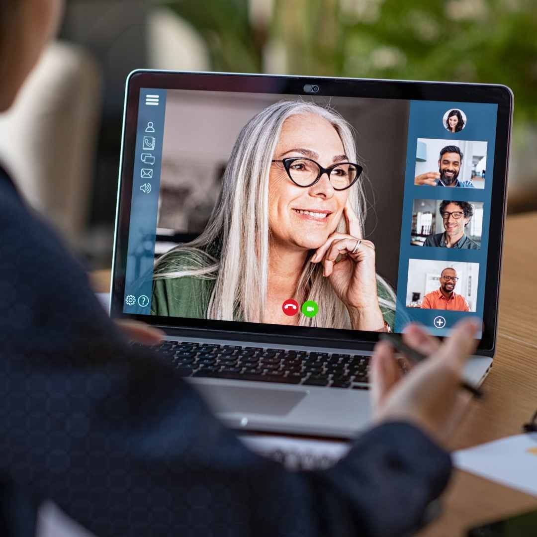 Person in a blazer on a video call with four others on a laptop screen; all are smiling.