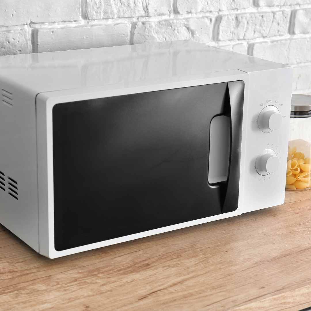 White microwave on a wooden countertop, with a black door. Brick wall background.