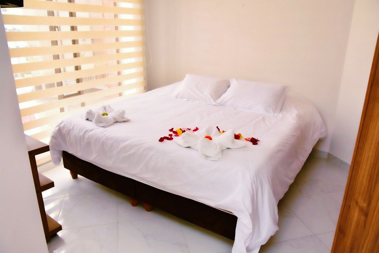 Bedroom with a white bed, two pillows, and floral decorations; window with blinds.
