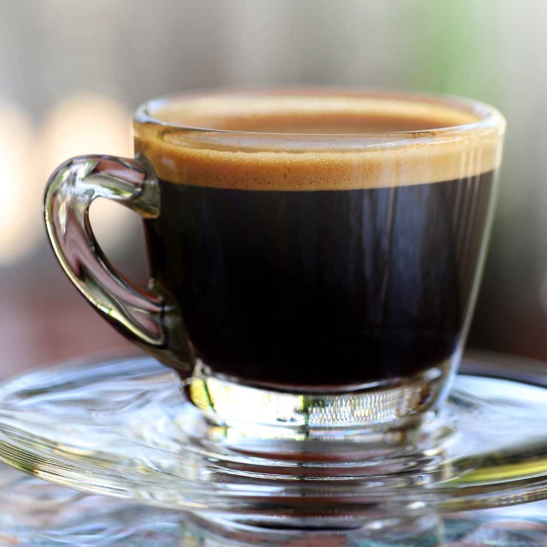 Espresso in a clear glass cup with a thick crema, on a glass saucer.