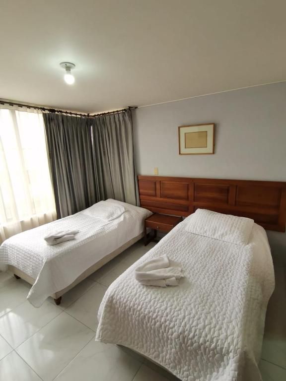 Two twin beds with white linens and towels in a hotel room with gray walls.