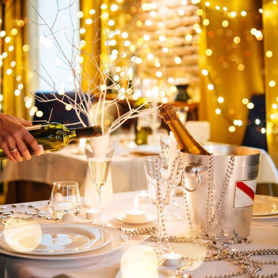Elegant dining table set for a celebration, with champagne bucket, lights, and a person pouring wine.