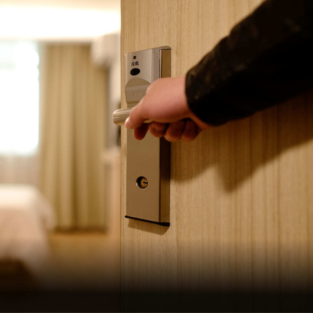Hand opening hotel door, entering a bedroom with a bed and curtains.