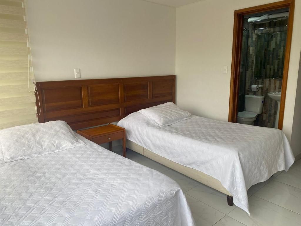Two twin beds with white bedding and a wooden headboard in a room; a bathroom is visible in the doorway.