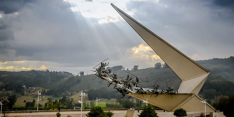 Monument against a cloudy sky with rays of sunlight, set in a mountainous landscape.