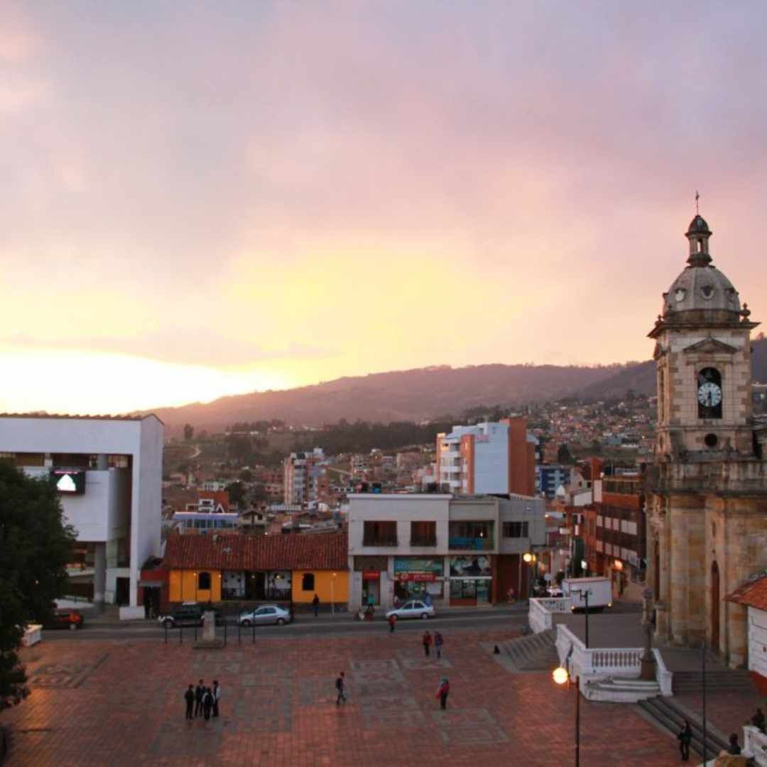 Town square at sunset with church steeple, buildings, mountains, and people.