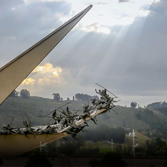 Monument with sculptures of figures against a cloudy sky, shafts of light.