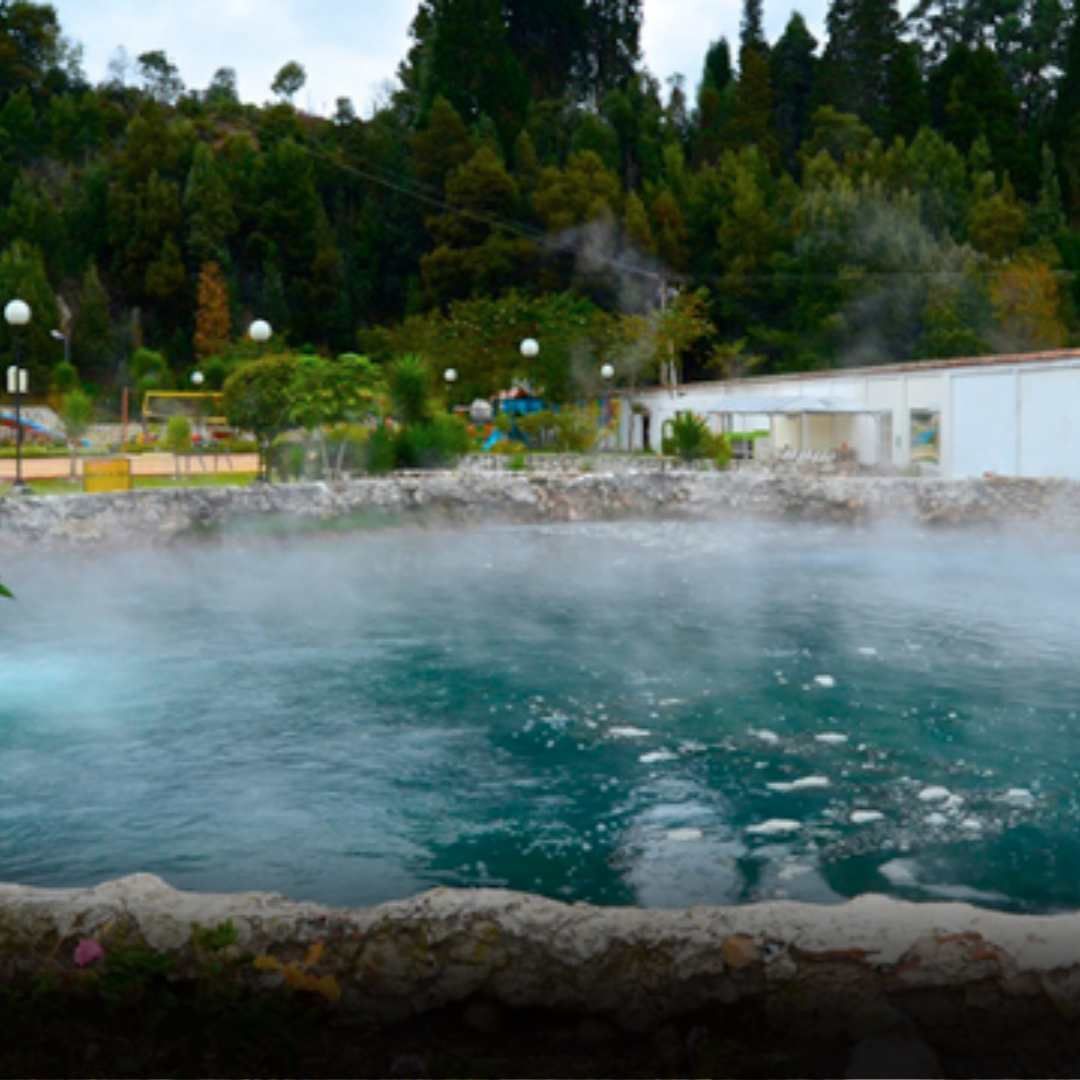 Steaming turquoise hot spring pool with a white building and trees in the background.
