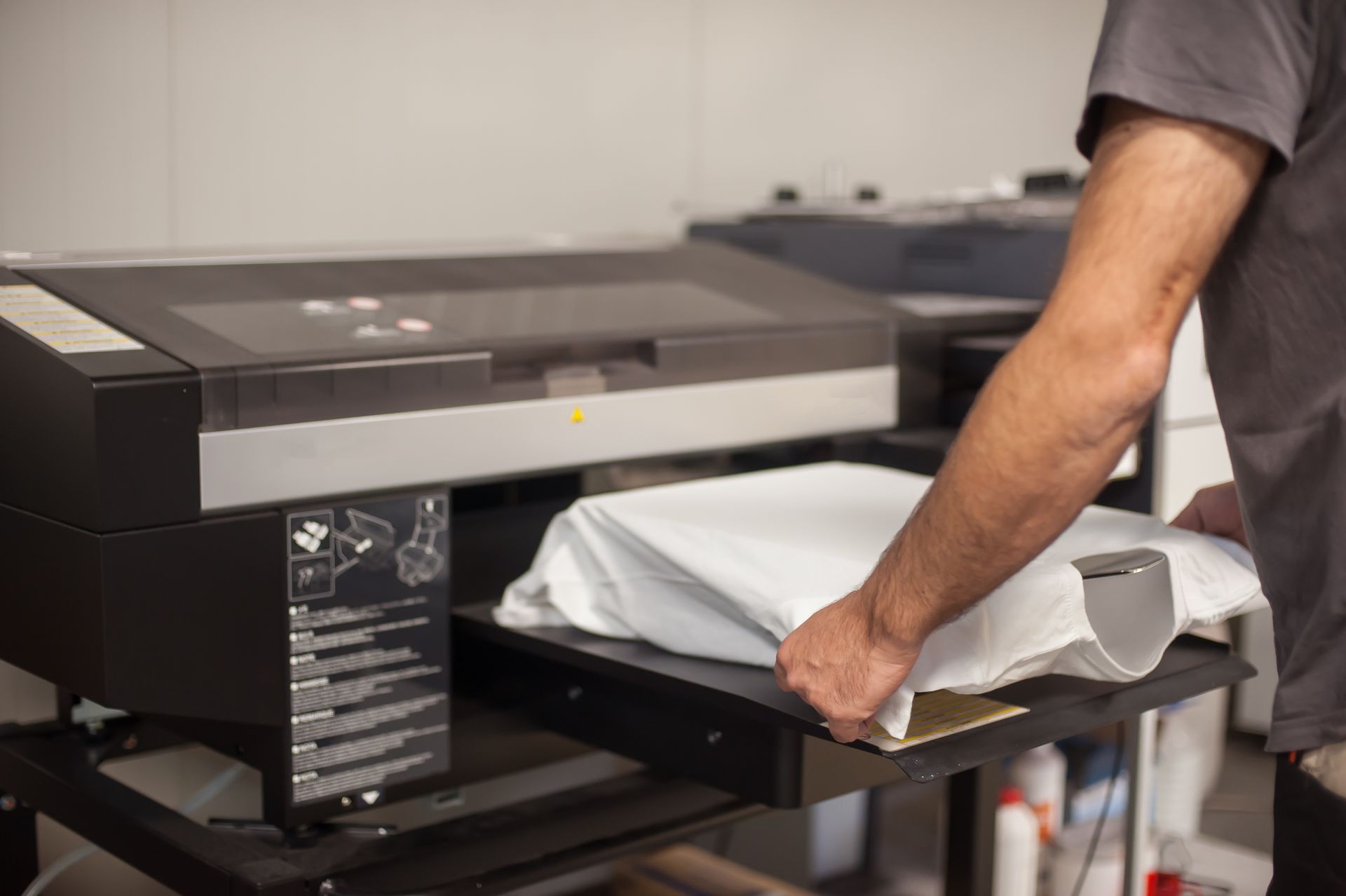 A person placing a white t-shirt onto a flatbed garment printer for direct-to-garment printing.