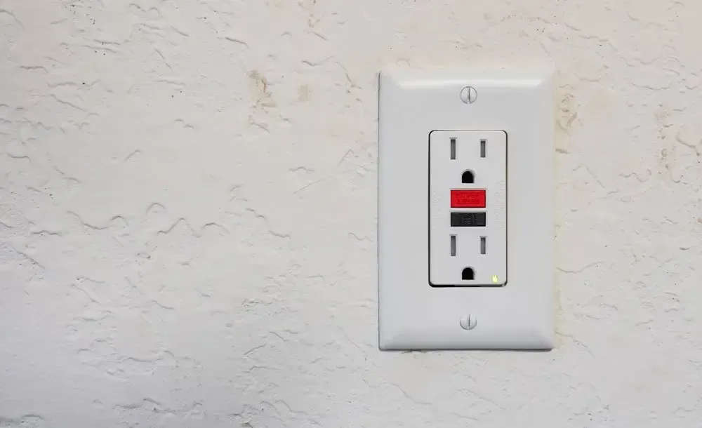 Wall outlet with a red and black GFCI reset/test switch on a white textured wall