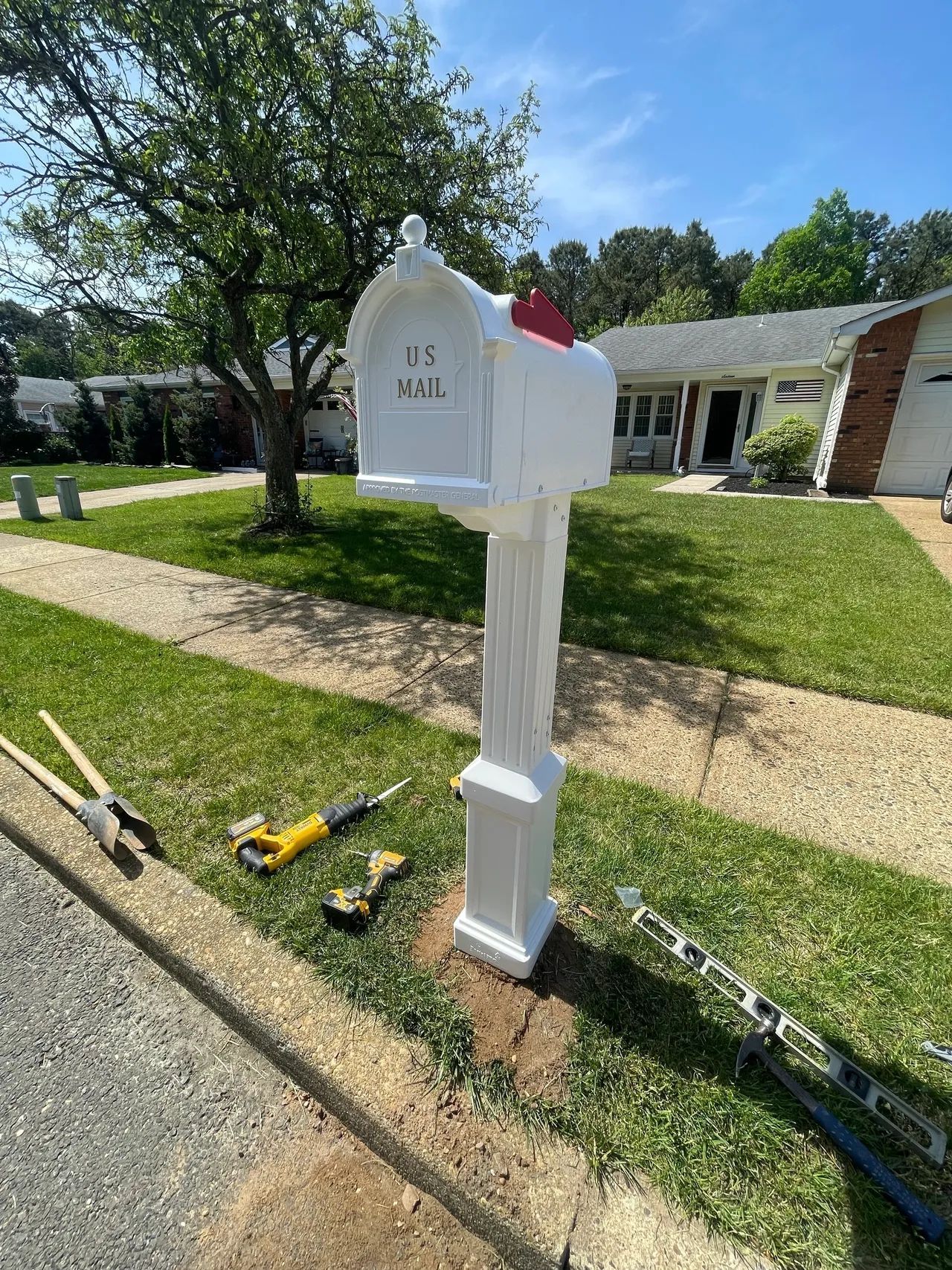 White mailbox on a suburban lawn with a driveway and tools on the grass nearby