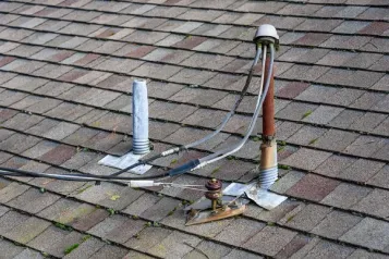 Roof with a small vent pipe, cable wires, and a vertical metal pipe on gray shingles.