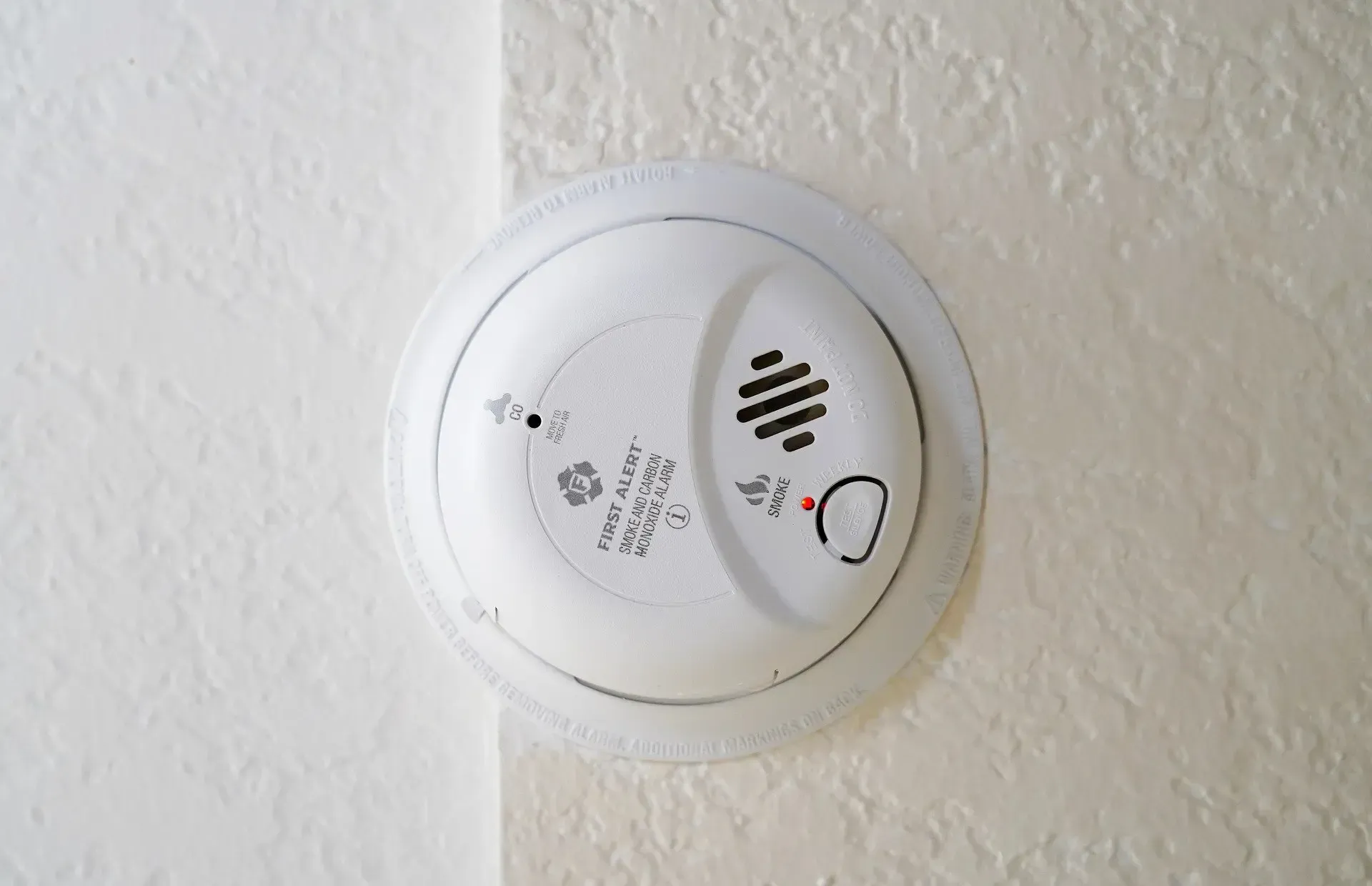 White wall-mounted smoke detector with test button on a textured wall
