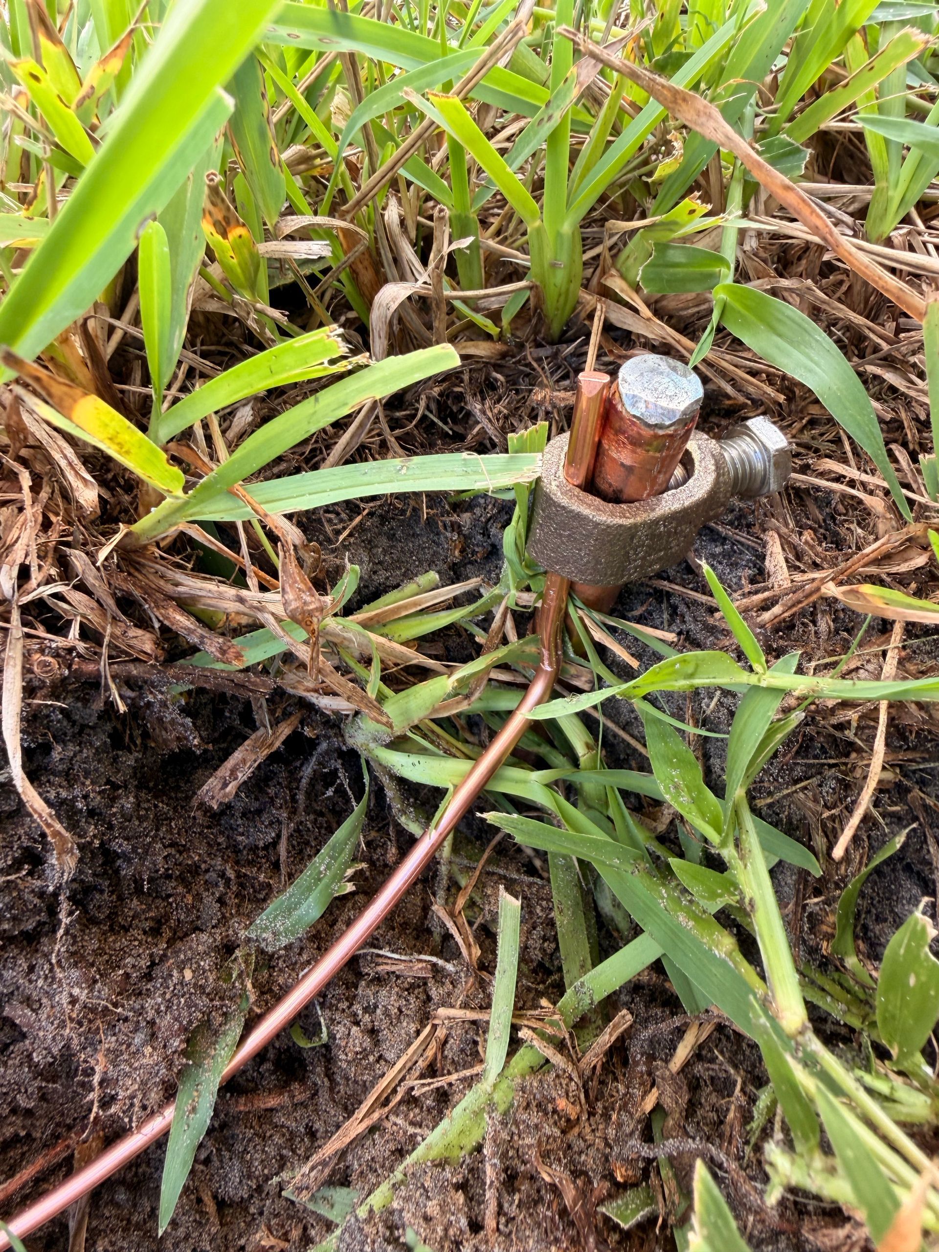 Close-up of a copper grounding conductor secured to a ground rod with a clamp.