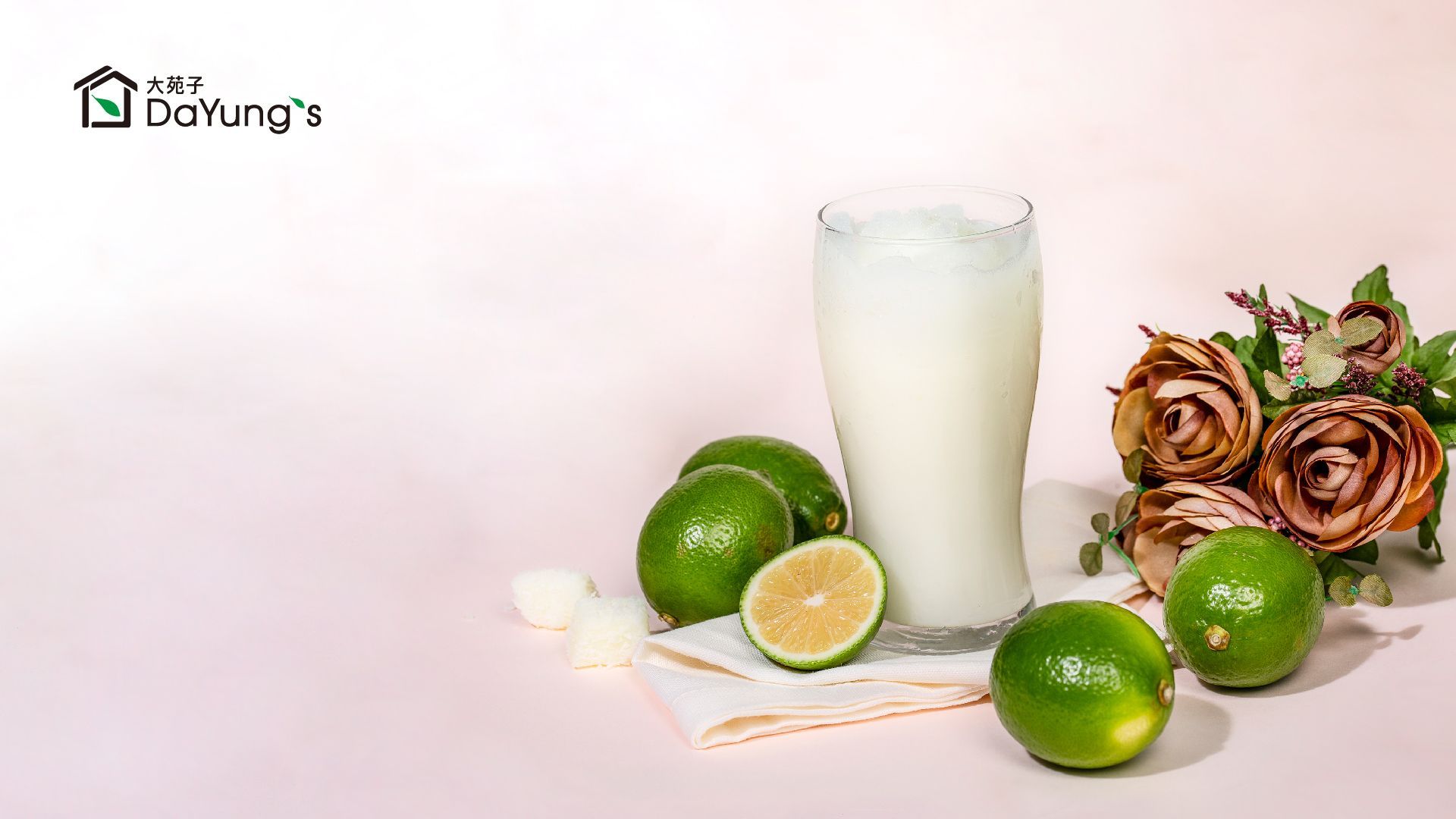 Lime juice with whole and sliced limes, a glass of milk, and decorative roses on a light background