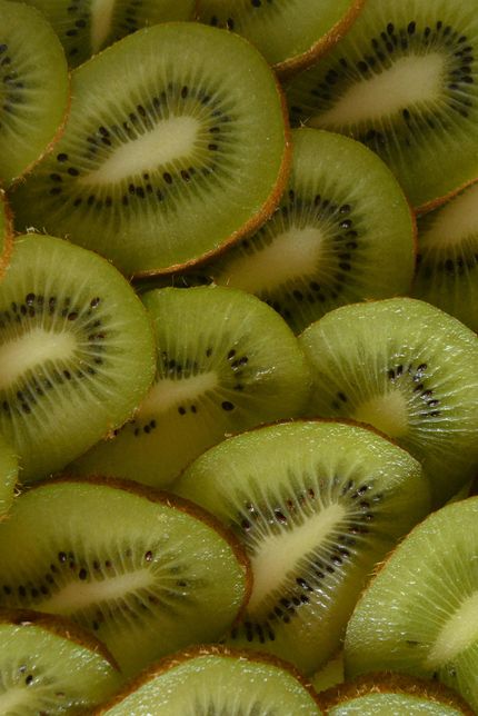 Slices of ripe kiwi fruit with bright green flesh and black seeds, closely arranged in a pile
