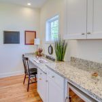 A kitchen with white cabinets and granite counter tops and a desk.