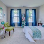 A bedroom with a bed , chair , ottoman and blue curtains.