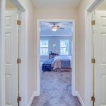 A hallway leading to a bedroom with a bed and a ceiling fan.